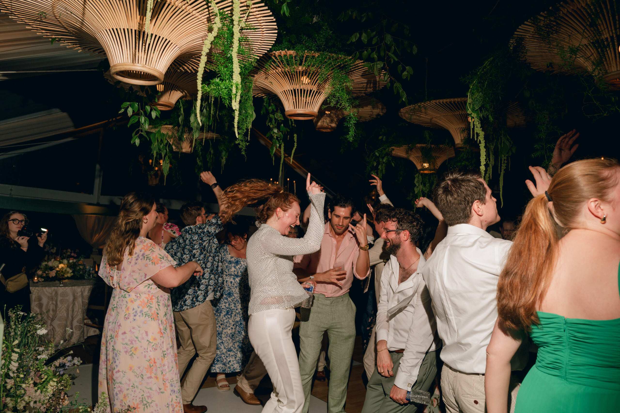 Wedding guests dancing together beneath woven pendant lights