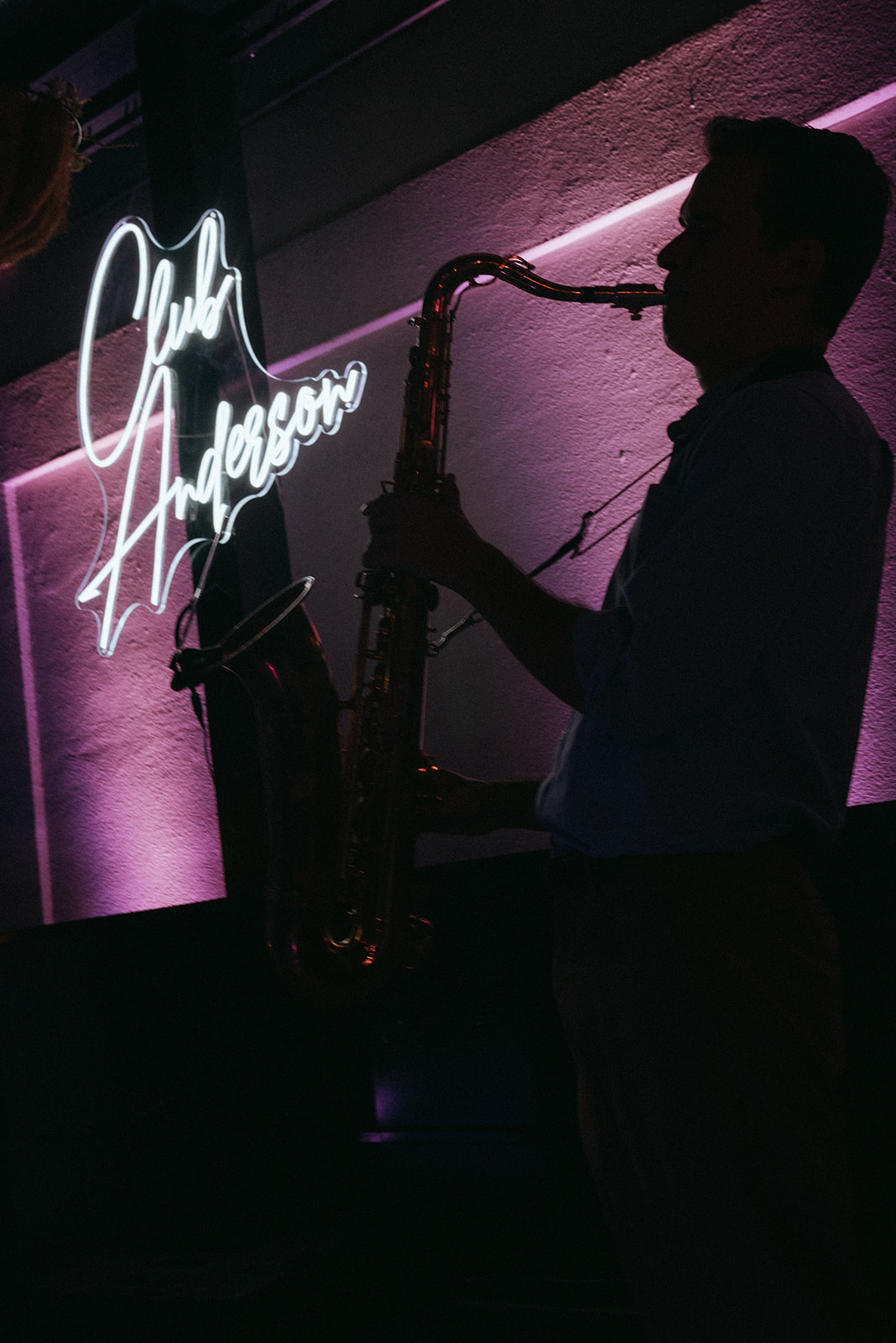 Saxophonist performing in silhouette against pink Reception lighting