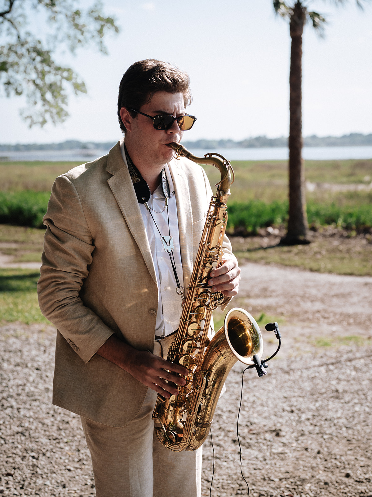 Saxophonist in a tan suit performing beside the marsh