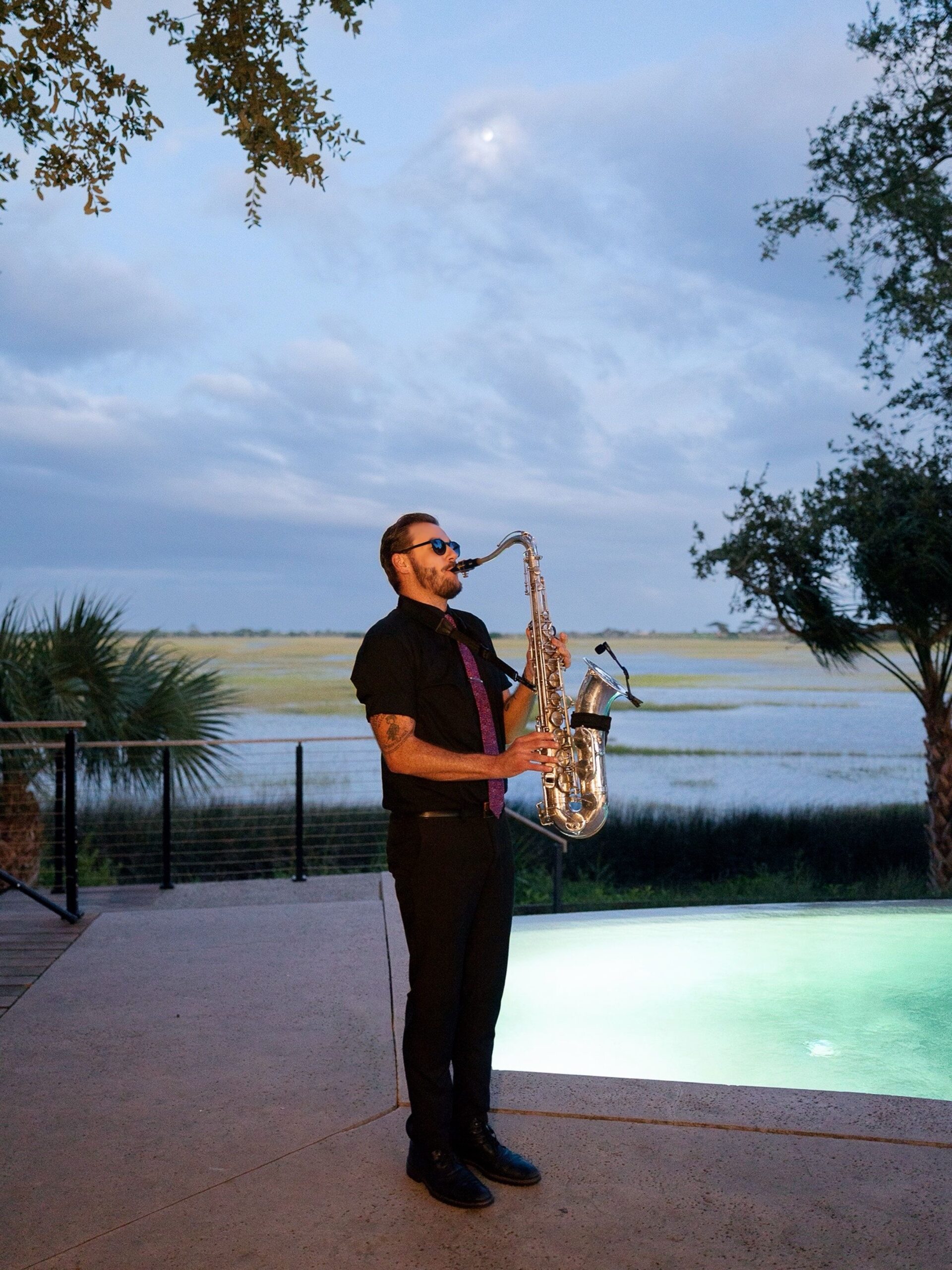 Saxophonist performing outdoors beside the waterfront at dusk